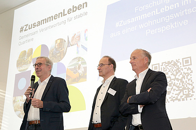 (v. li.) Klaus Leuchtmann (EBZ-Vorstandsvorsitzender), Dr. Christian Lieberknecht (GdW-Vorstand) und Alexander Rychter (VdW-Verbandsdirektor) begrüßen die Teilnehmerinnen und Teilnehmer zur zweiten Fachtagung „Quartiere der Zukunft – Von Überforderung zu Resilienz“. Bildquelle: EBZ/Andreas Molatta.